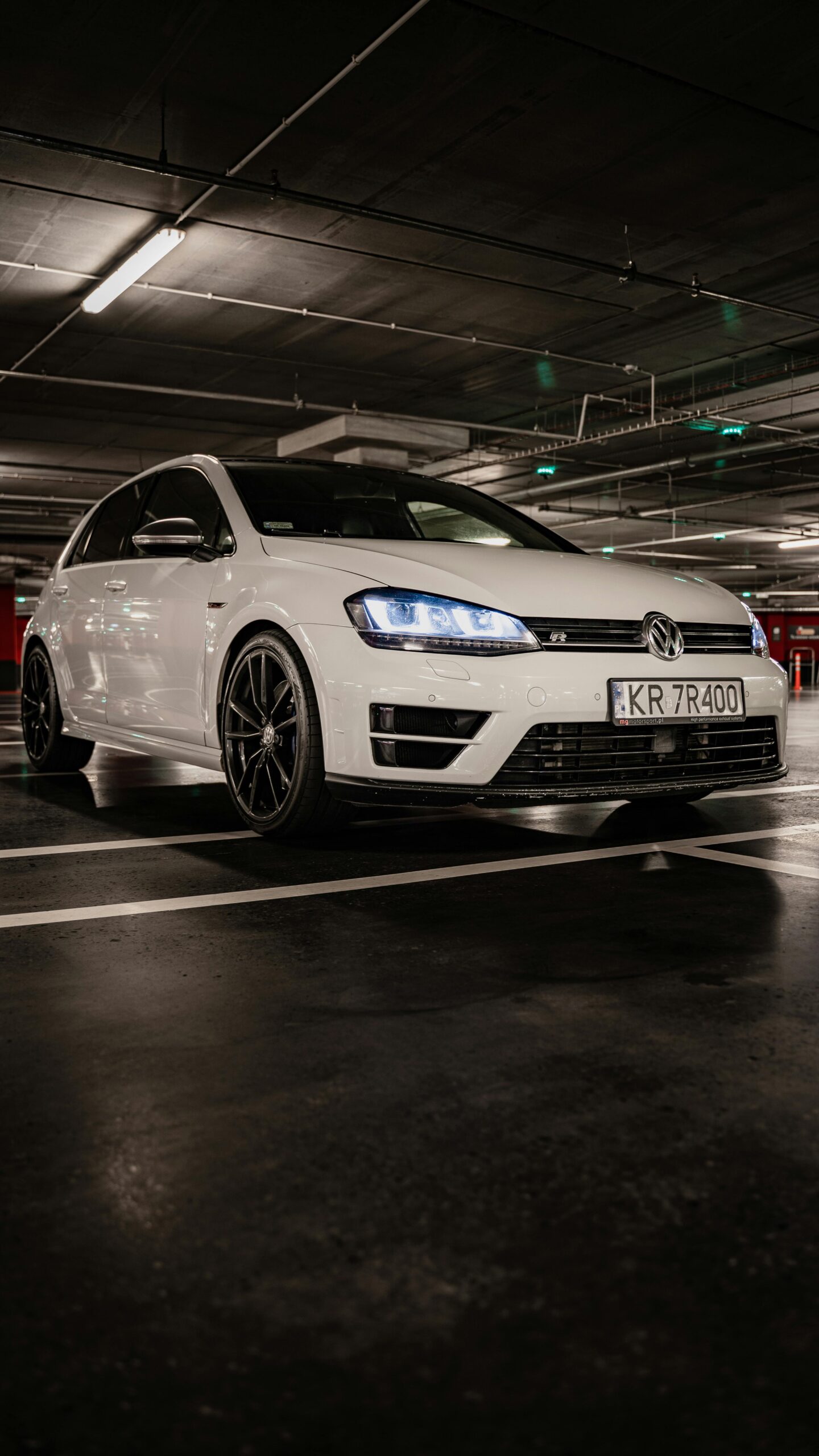 Dynamic low-angle shot of a white Volkswagen vehicle in an underground parking garage in Kraków.
